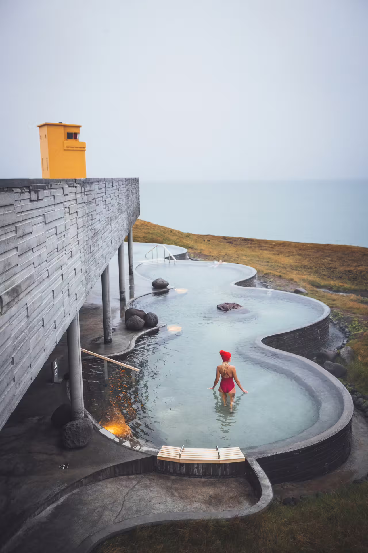 Woman in red swimsuit wading in Geosea geothermal sea baths with ocean views in Iceland