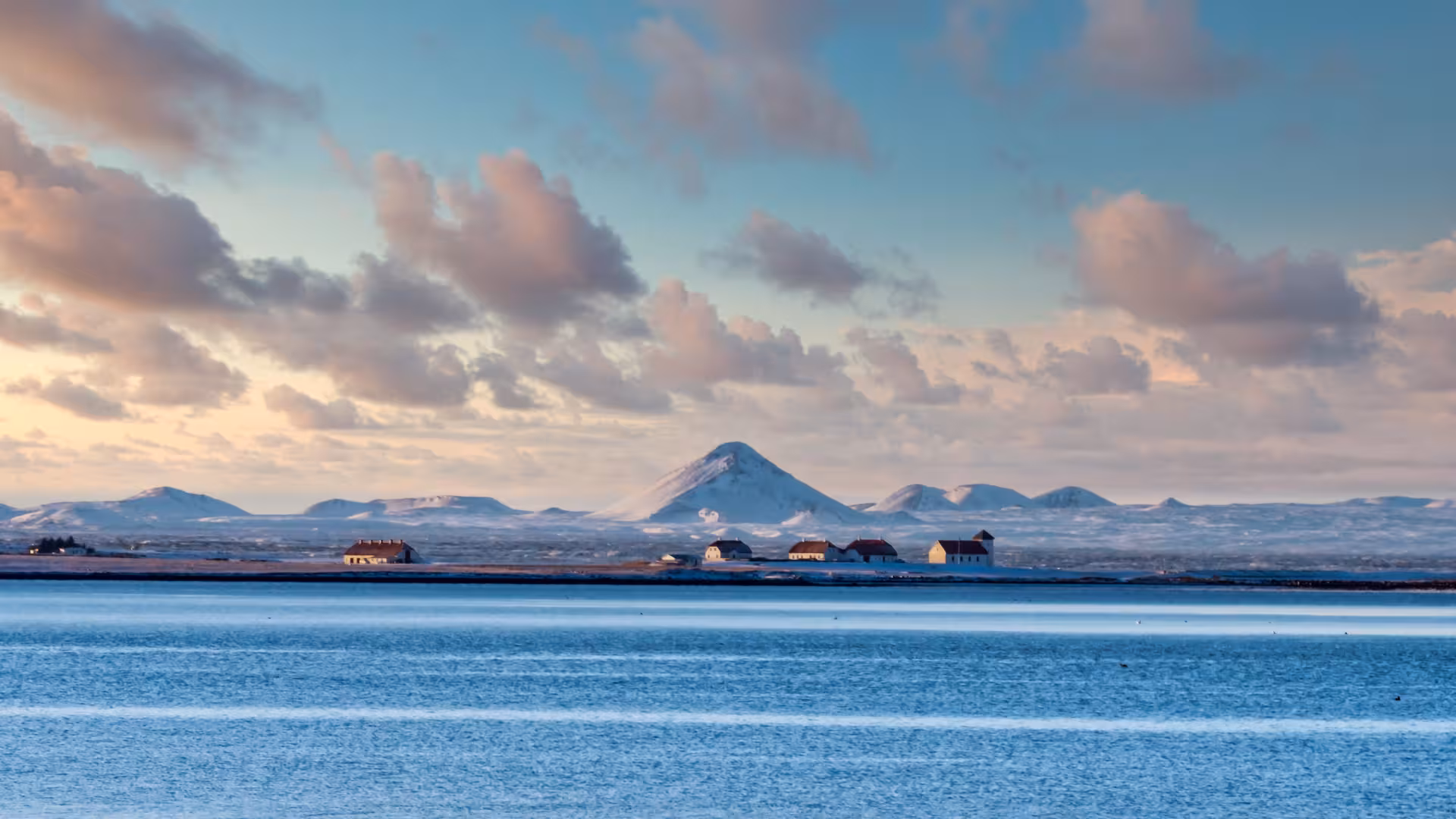 Coastal view toward snow-dusted volcanic peaks near Krýsuvík, Iceland, on a geothermal sprint tour