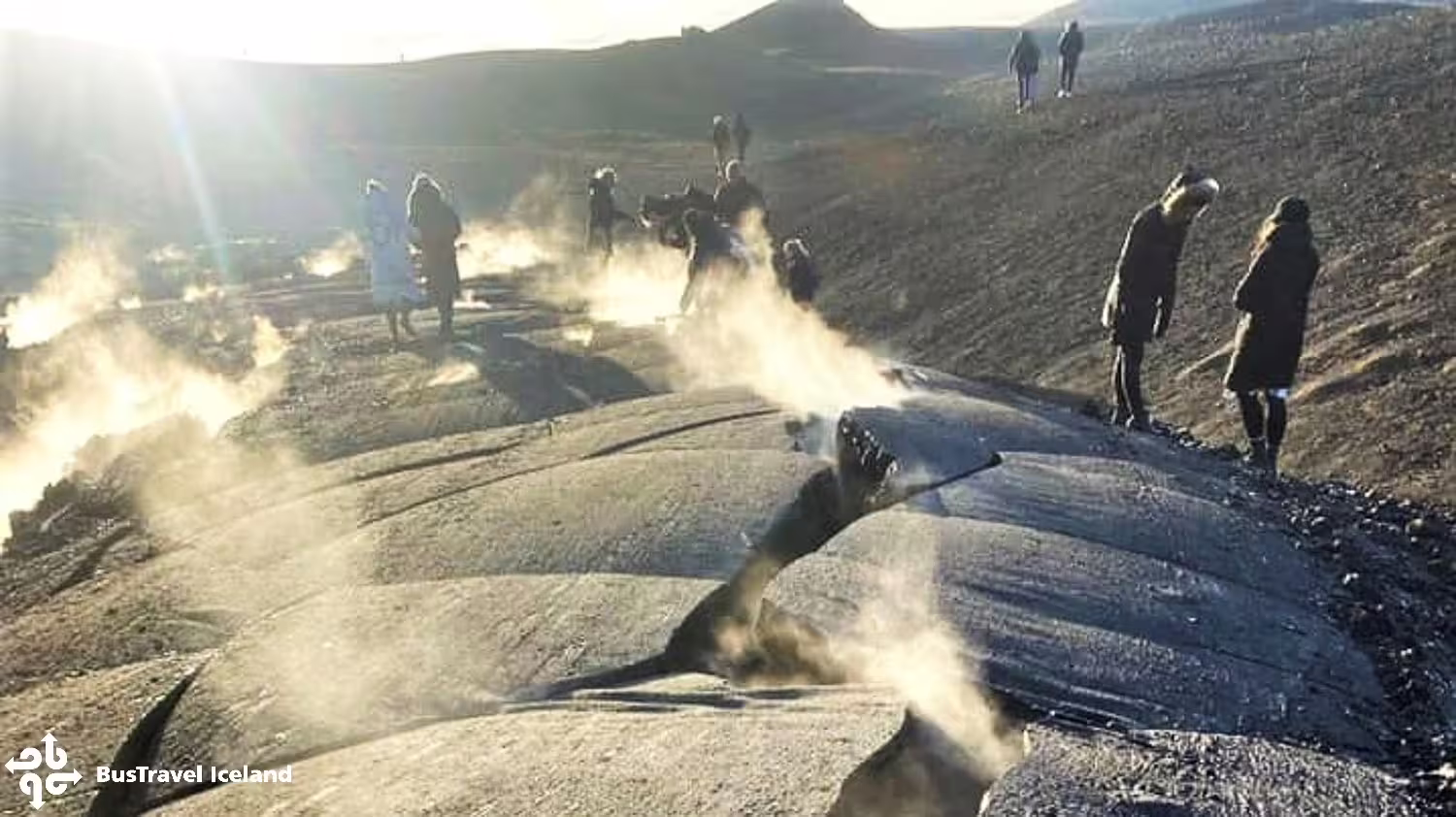 Tourists walking on volcanic terrain with geothermal steam vents near Reykjavik, Iceland