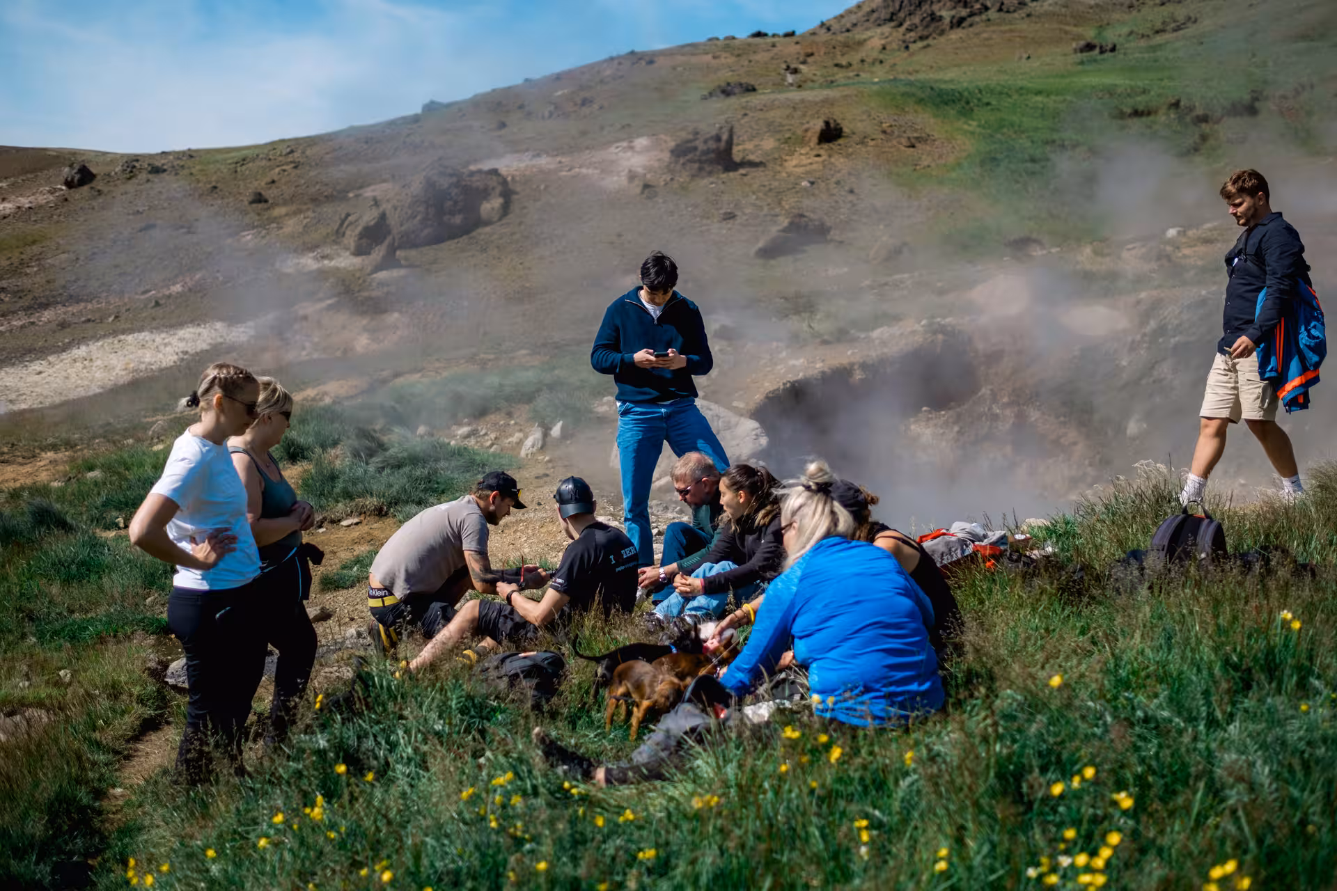 Group of hikers resting on grassy hillside near geothermal steam vents at Hengill volcano Iceland