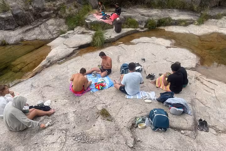 Visitors relaxing on rocks by a serene lagoon in Geres National Park, enjoying a picnic and natural bathing experience.