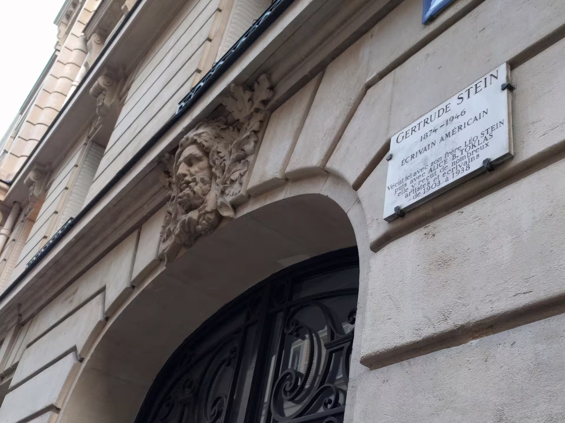 Gertrude Stein commemorative plaque on Paris building facade with stone arch and carved face