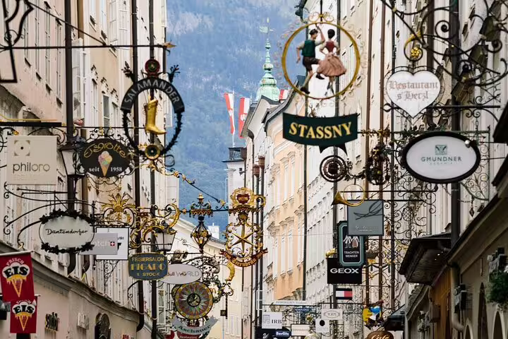 Ornate hanging shop signs along Getreidegasse street in Salzburg old town with mountain backdrop