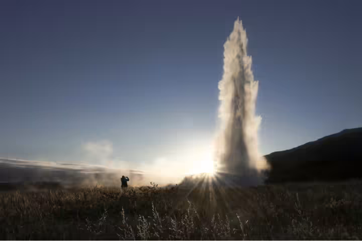Geyser erupting at sunset on Iceland's Golden Circle with silhouetted visitor in foreground