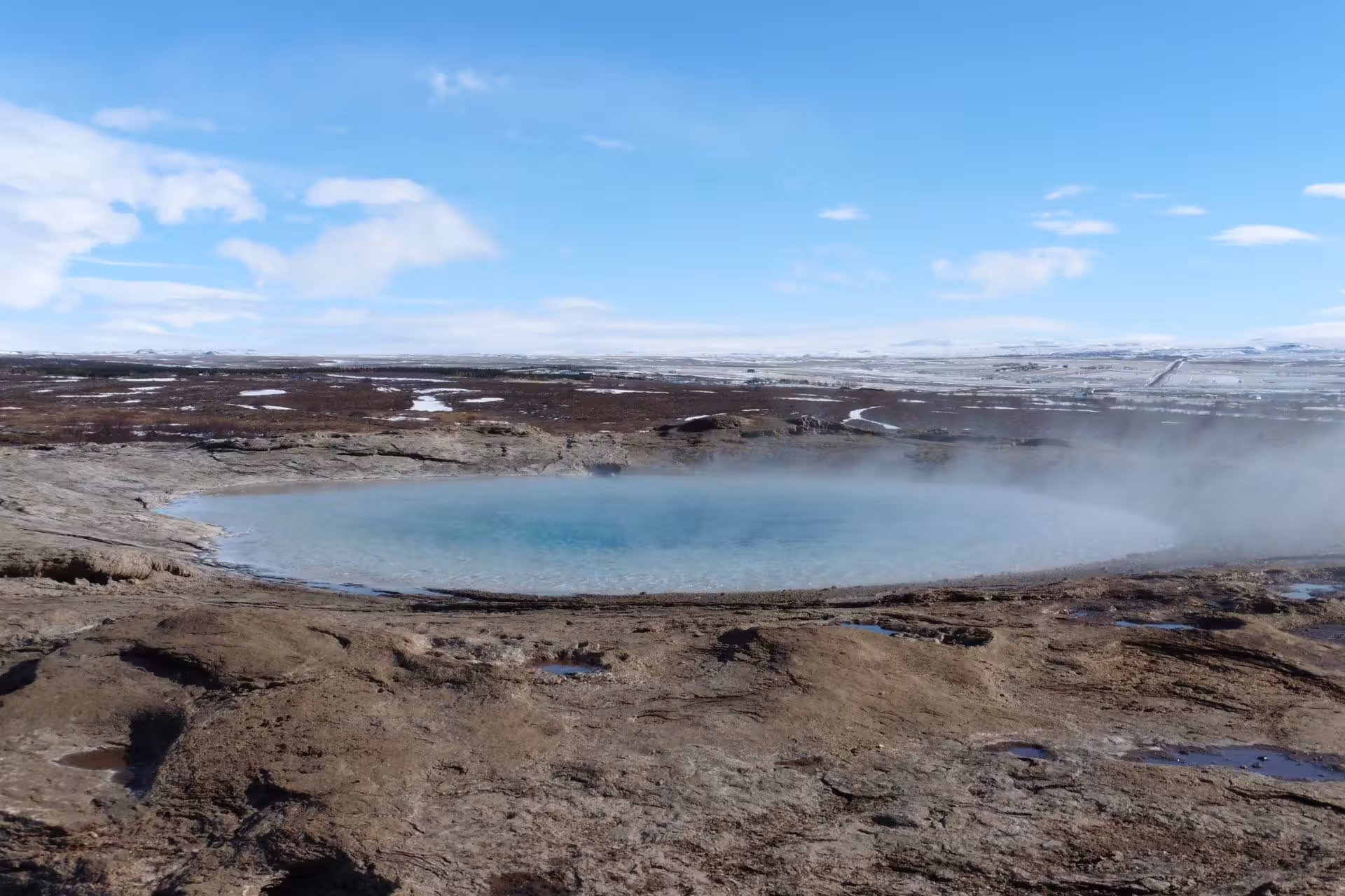 Steaming geothermal hot spring pool at Geysir geothermal area, Iceland, with snowy landscape in background