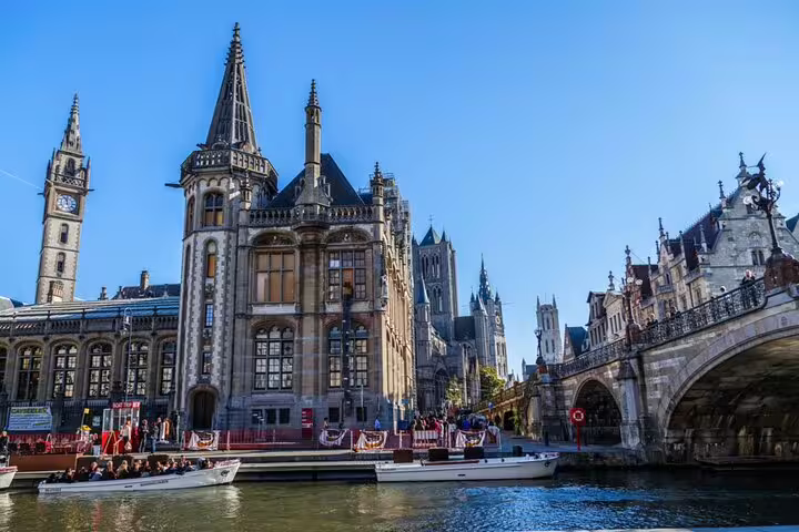 Historic Ghent city center canal with Gothic architecture, bridge, and tour boats on a sunny day