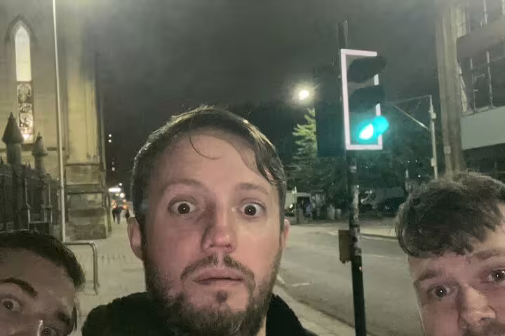 Three men making surprised faces on a city street at night with a green traffic light