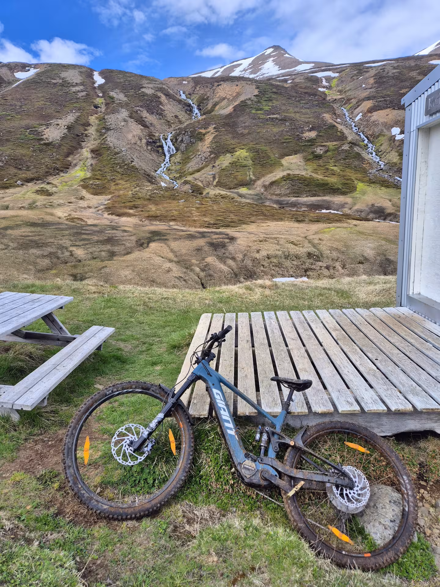 Giant e-MTB mountain bike leaning on wooden deck with snowy mountain peaks and waterfall in background