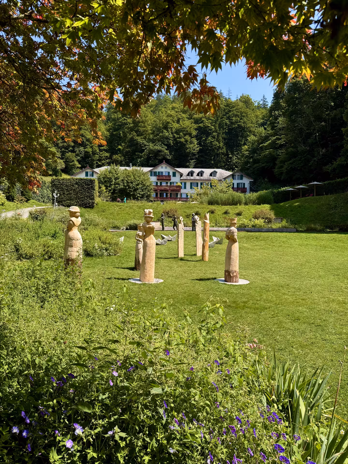 Giessbach gardens with carved statues and lake-view hotel, scenic stop on Iseltwald Giessbach e-bike tour