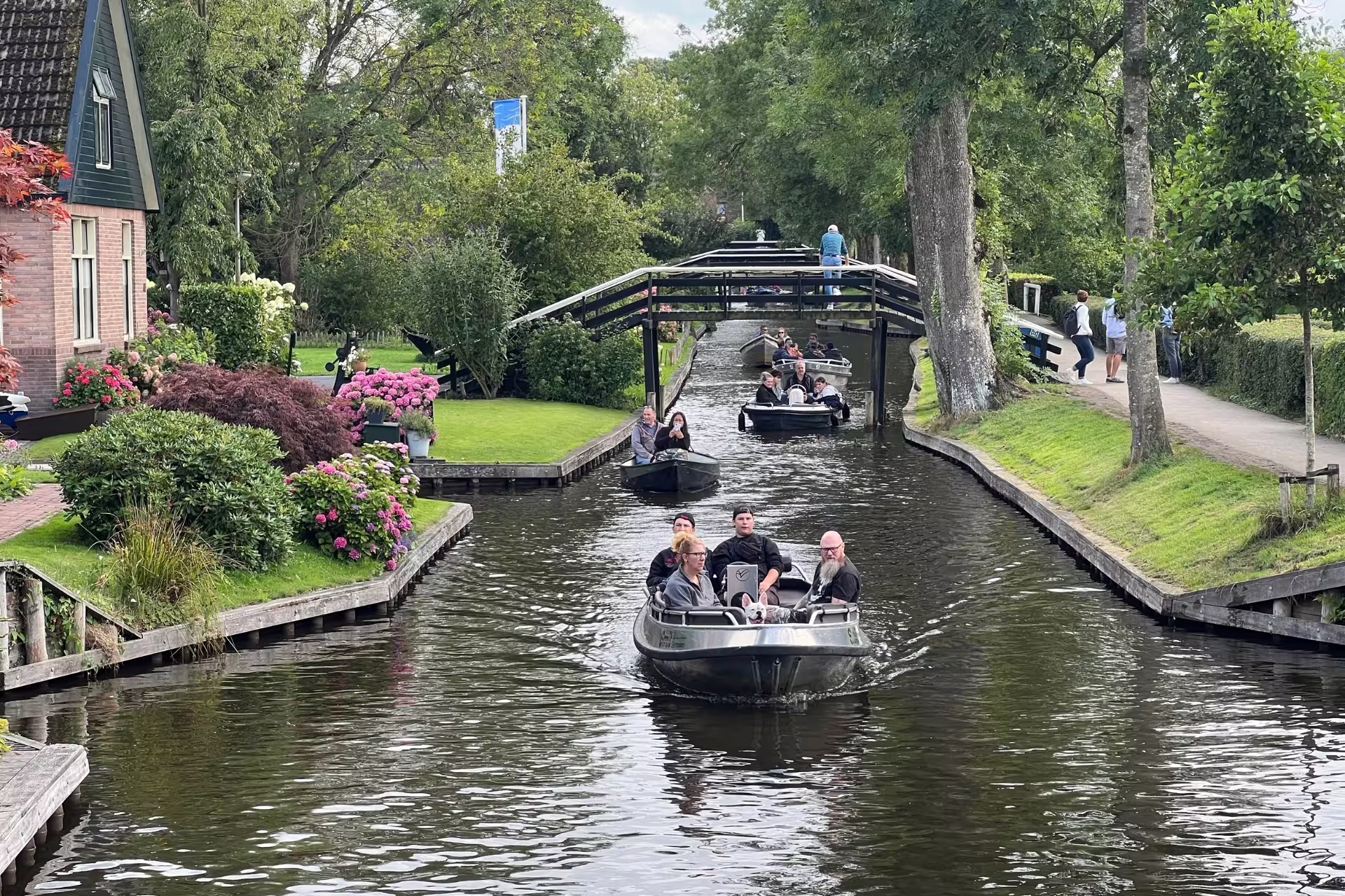 Boats cruising Giethoorn canals under a small bridge, scenic stop on Amsterdam Keukenhof and Giethoorn tour