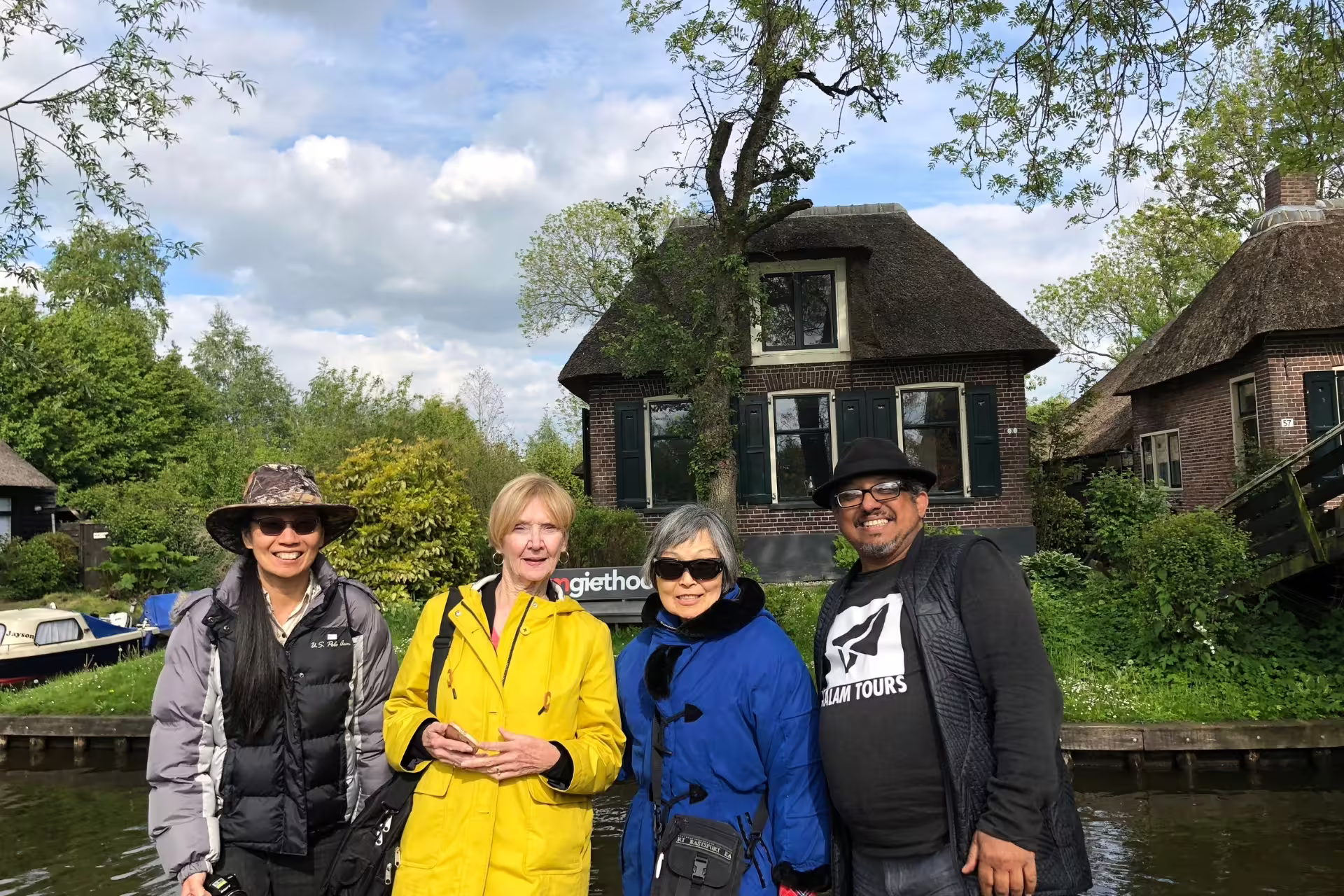 Travelers pose by a Giethoorn canal and thatched cottage on Amsterdam day trip with canal cruise
