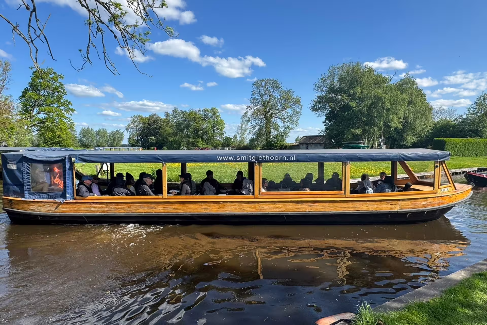 Covered boat with passengers on Giethoorn canal cruise, part of Amsterdam day trip to Zaanse Schans