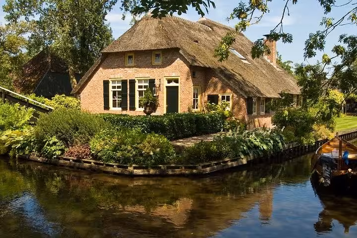 Thatched-roof farmhouse on Giethoorn canal with lush greenery, ideal stop on private tour and boat trip
