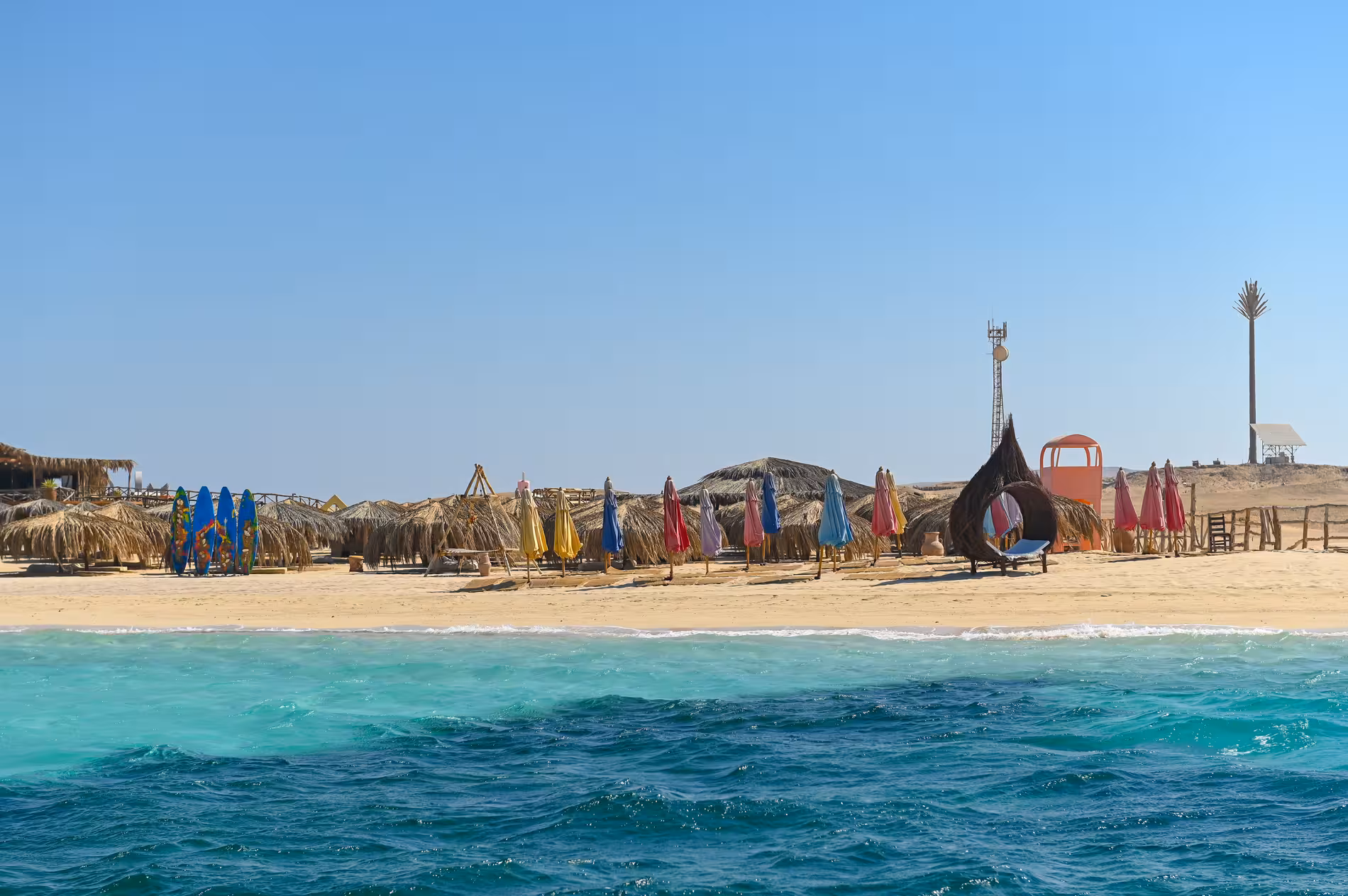 Colorful beach umbrellas and thatched huts on Giftun Island's sandy shore with turquoise Red Sea waters