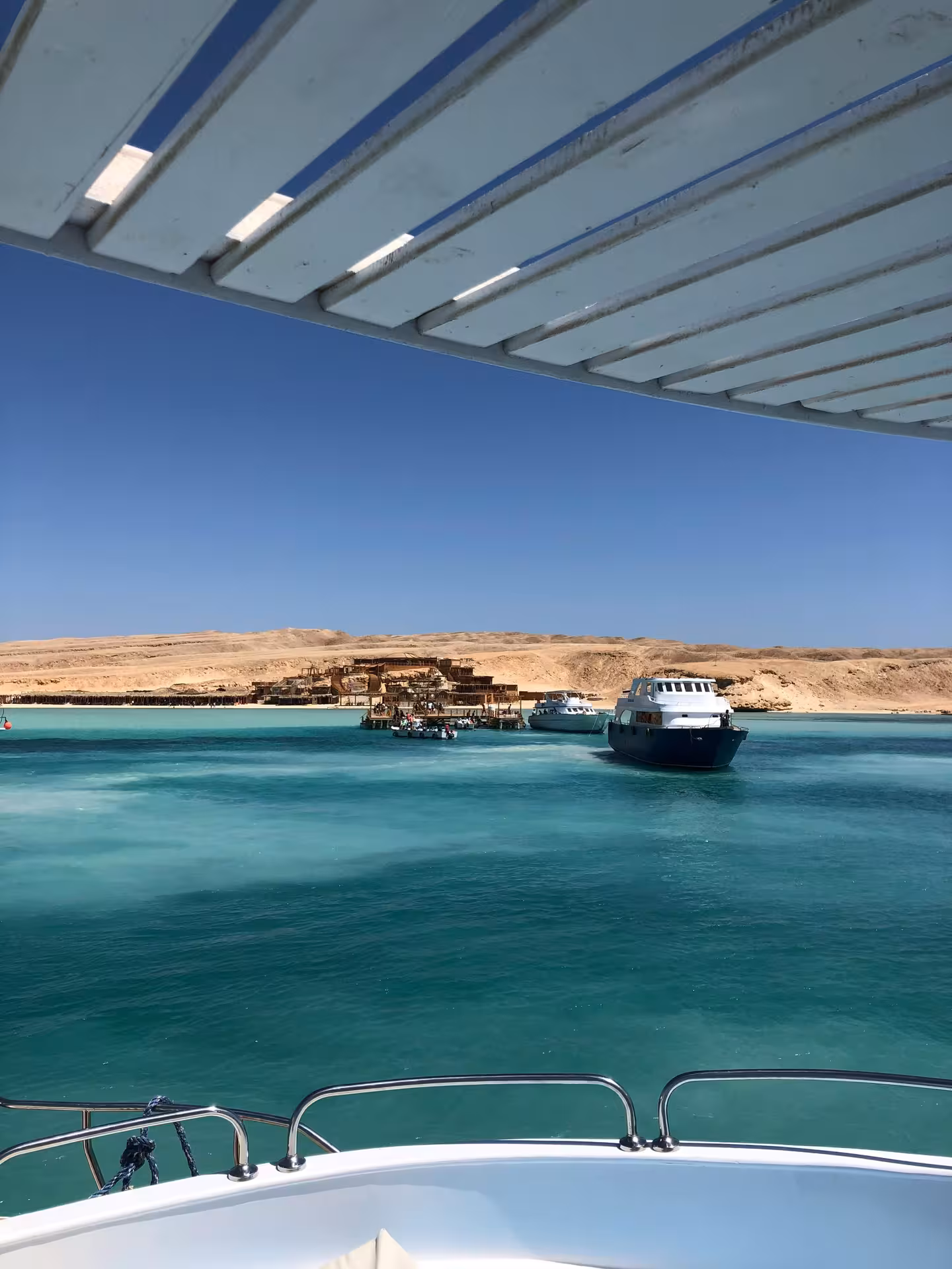 Turquoise waters of Giftun Island with boats docked near a sandy shore and wooden pier structures