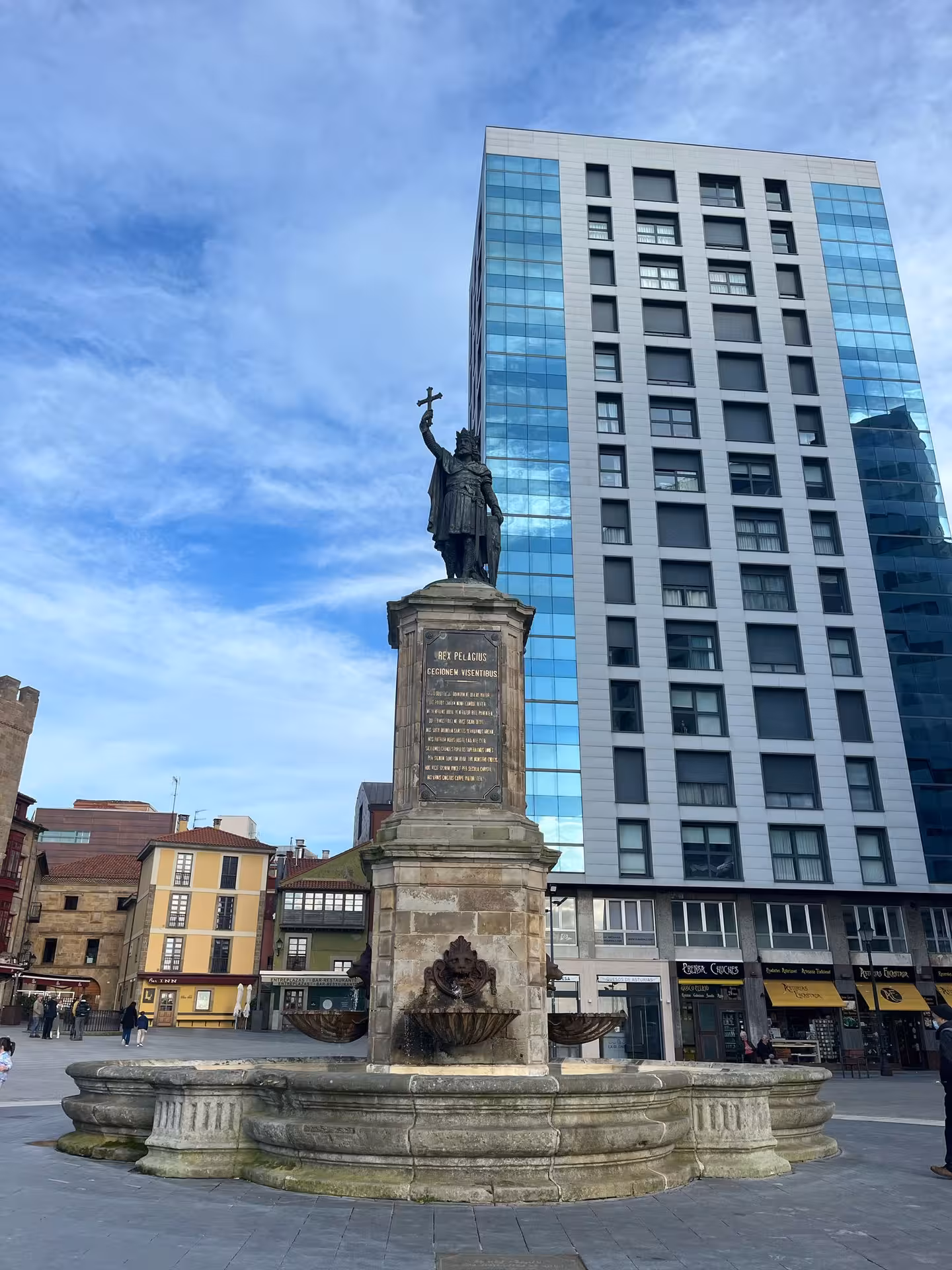 Statue of Pelayo with modern buildings in Gijon's city center, a highlight of the Cultural City Bus Tour Experience.