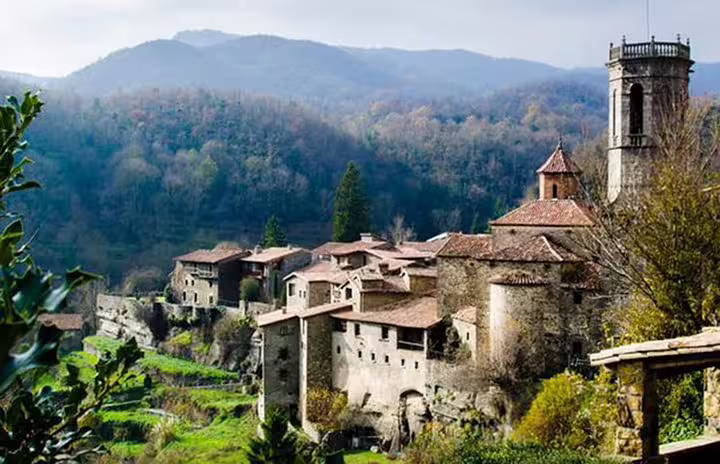 Medieval village in Catalonia with stone buildings nestled in lush green hills, showcasing historic charm and scenic views.
