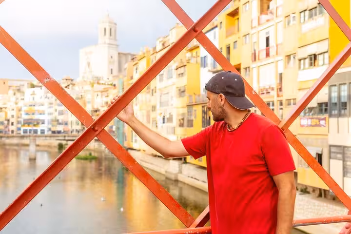 Man in red shirt admires colorful riverside buildings from Eiffel Bridge during Girona's private city walk tour.