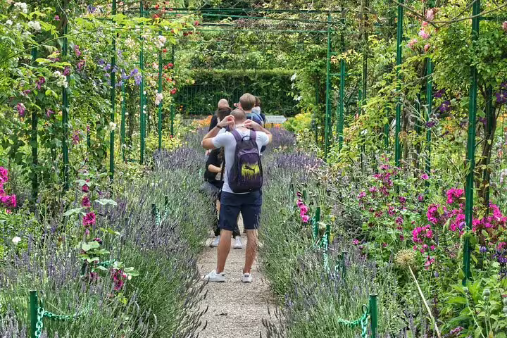 Tourists walking through flower-lined garden path at Monet's Giverny with lavender and roses