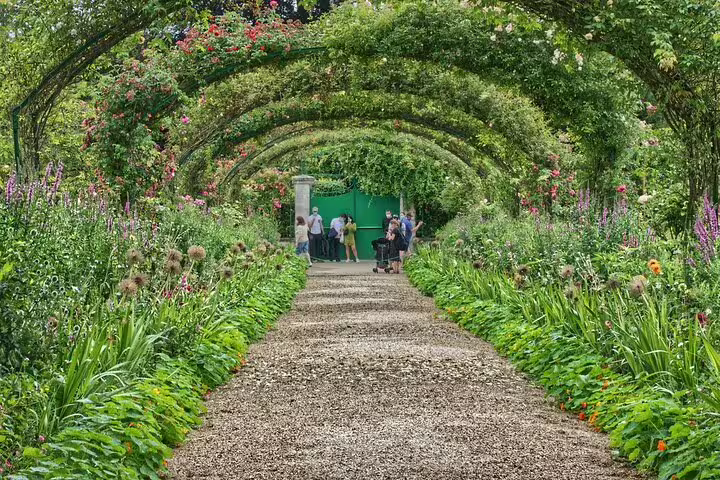 Lush rose-covered archway tunnel along gravel path in Monet's garden at Giverny with visitors