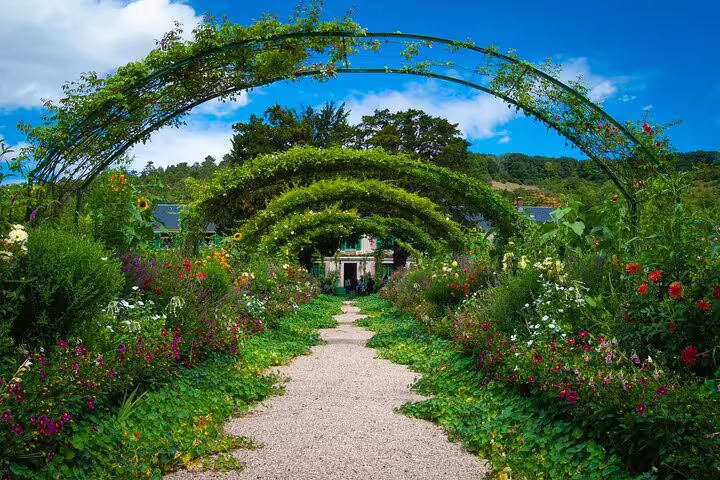 Flower-lined gravel path with green arched trellises leading to Monet's house in Giverny gardens