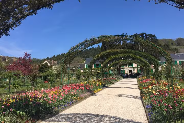 Flower-lined gravel path with green arches leading to Monet's house in Giverny garden, Paris day trip