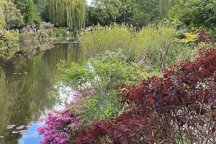 Monet's lily pond garden at Giverny with colorful flowers and weeping willows reflected in calm water