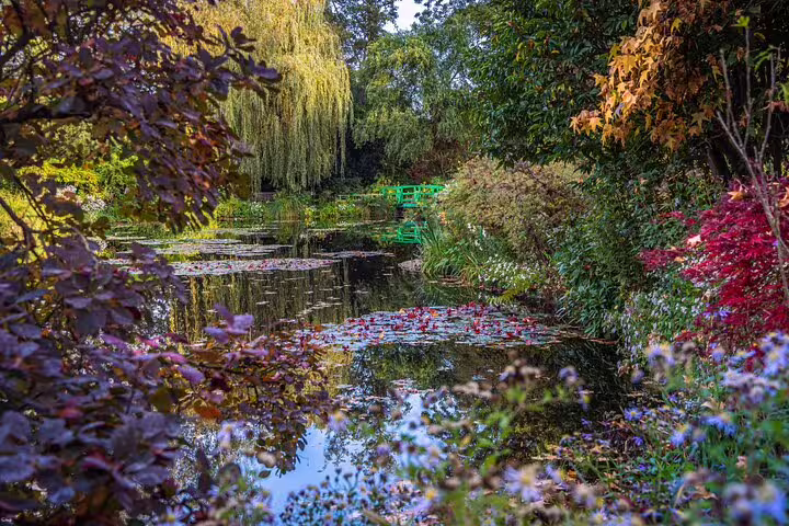Monet's water lily pond with green Japanese bridge surrounded by colorful autumn foliage in Giverny