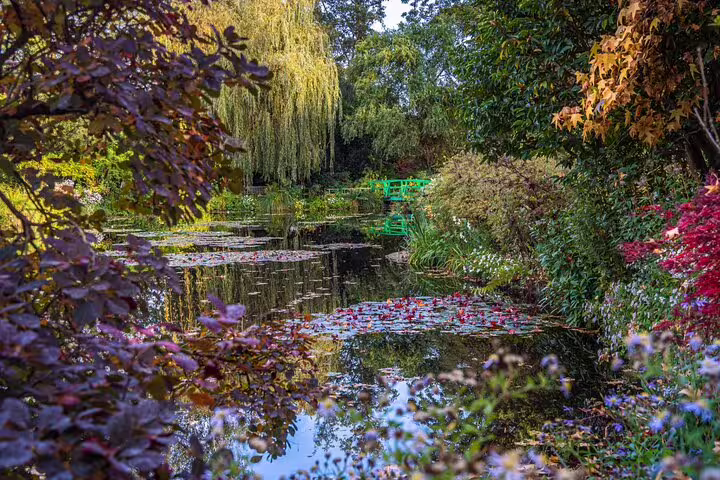 Monet's water lily pond with green Japanese bridge surrounded by colorful autumn foliage in Giverny
