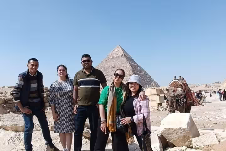 Tourists standing in front of the Pyramid of Giza with a camel nearby on a guided excursion.