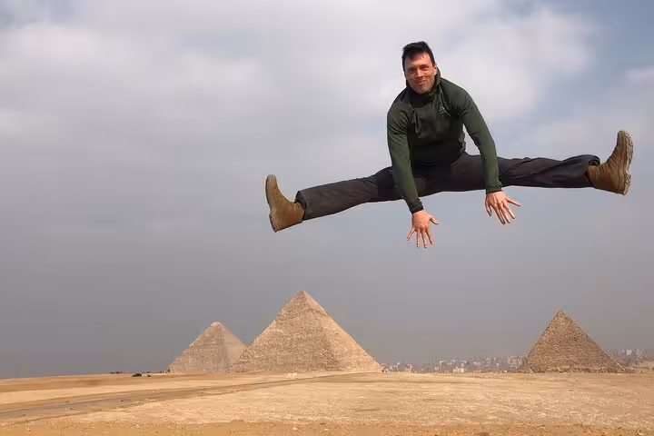 Traveler jumps in front of Giza Pyramids desert view on private tour with ATV ride, camel trek and cruise
