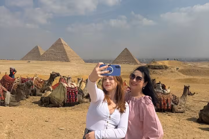 Travelers taking a selfie by camel caravan with the Giza Pyramids in background, Cairo sightseeing tour