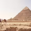Camel and handler standing before the Great Pyramid of Giza on a clear desert day