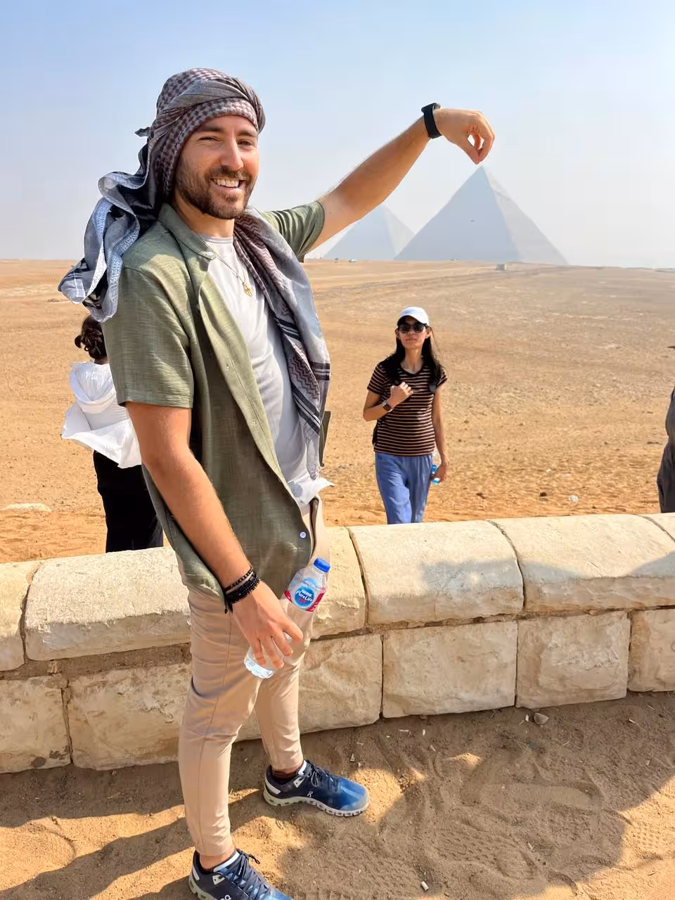 Tour guest in keffiyeh posing with Giza Pyramids backdrop on Cairo camel ride and lunch tour photo stop