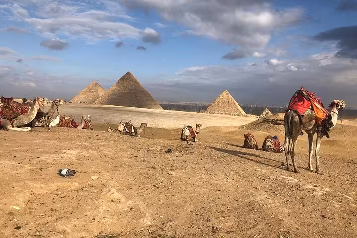 Camel rest area facing the Giza Pyramids under dramatic skies, part of an all-inclusive camel ride tour