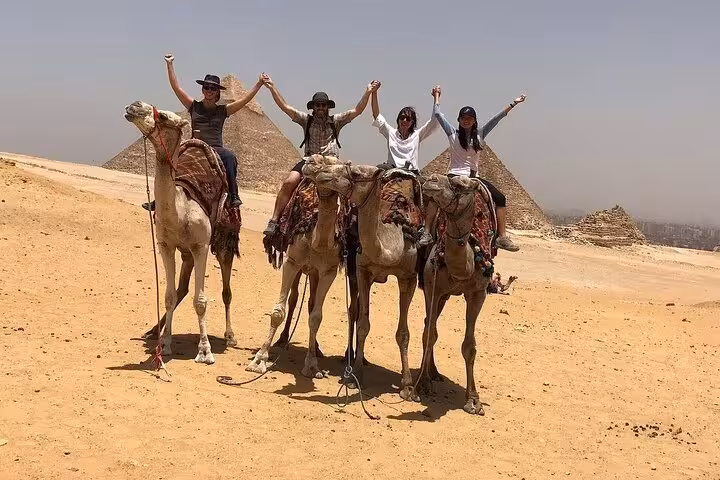 Group enjoying free camel ride on a half-day private Giza Pyramids tour in Egypt desert panorama