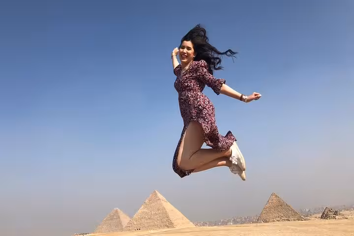 Traveler jumping with Giza Pyramids behind on all-inclusive Giza tour with pyramid entry and camel ride