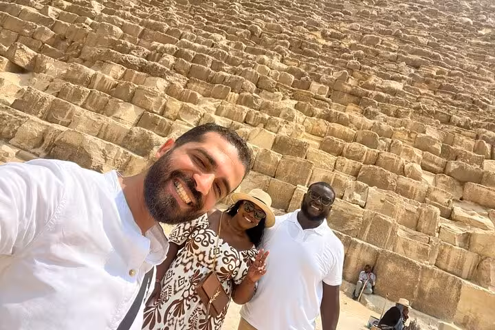 Happy travelers selfie beside the Great Pyramid stones on a private Giza tour with camel ride and ATV