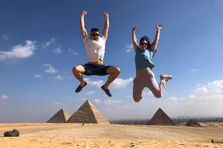 Couple jumping with Giza pyramids in the background on a private Cairo tour with ATV ride, camel trek and cruise