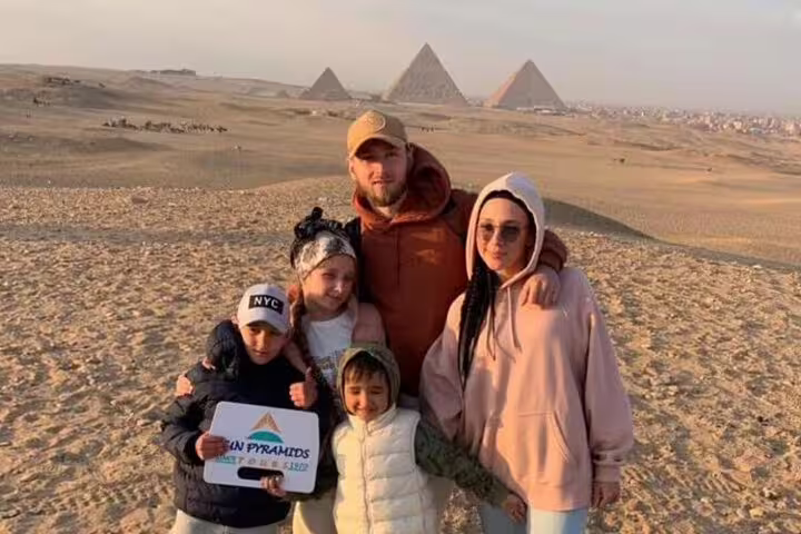 Family photo on Giza Plateau at sunset with the pyramids in the distance on a private Cairo day tour
