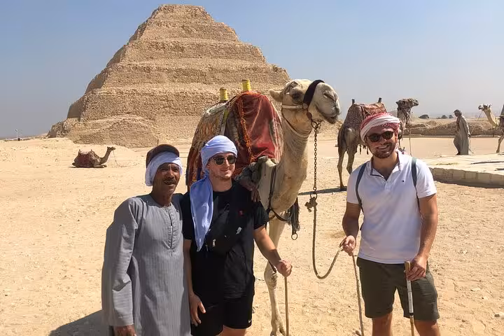 Group photo with camel and Saqqara Step Pyramid on guided all-inclusive Giza Pyramids, Memphis and Saqqara trip