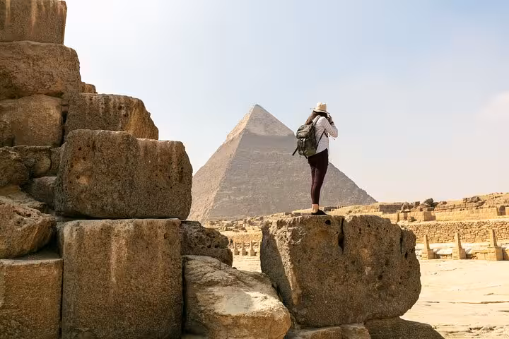 Visitor photographing the Great Pyramid from stone blocks on Giza Plateau with skip-the-line entry ticket access