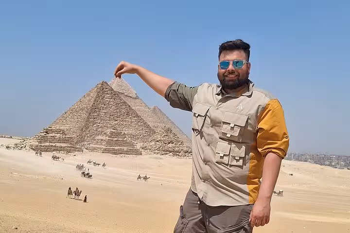 Tourist playfully poses with the Giza Pyramids backdrop on a private tour including Sphinx, Memphis, Saqqara, and camel ride.