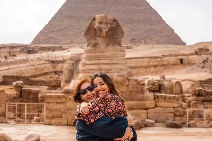 Travelers hugging at the Great Sphinx with Giza pyramid behind, private guided tour with transfers and tickets