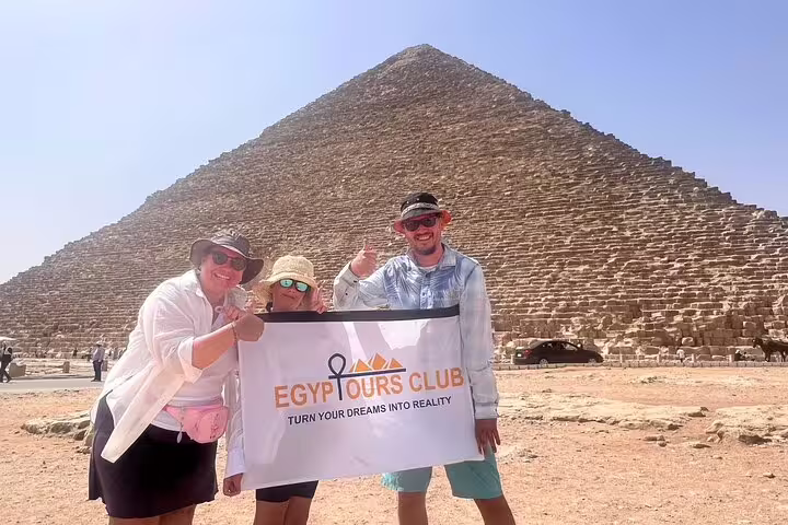 Travelers holding Egypt Tours Club banner in front of the Great Pyramid of Khufu on a half-day Giza tour