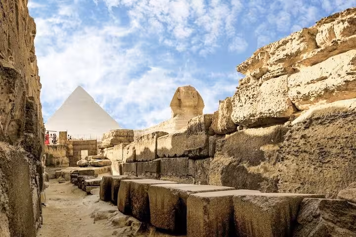 Path between limestone blocks at Giza with Sphinx and pyramid views on Grand Egyptian Museum day tour lunch