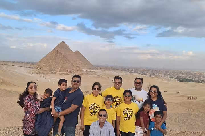 Group of tourists smiling in front of the Giza Pyramids, enjoying a private tour with camel rides and lunch.