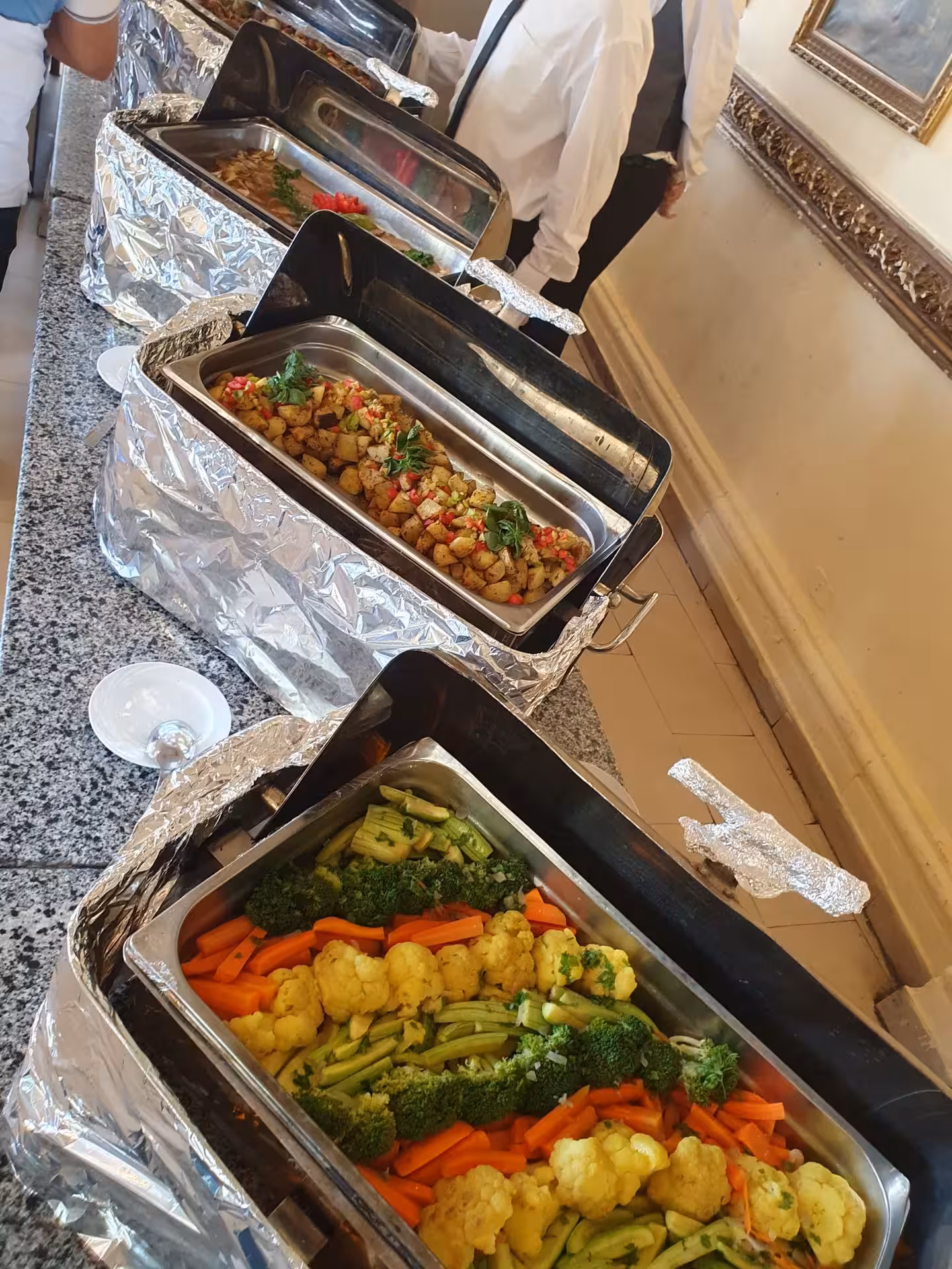 Buffet spread with steamed vegetables, roasted potatoes, and mixed dishes served in chafing trays at a catered event
