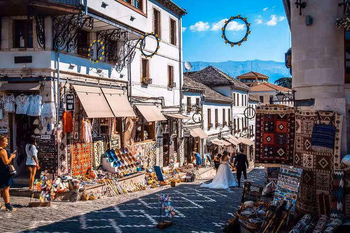Explore the vibrant bazaar in Gjirokastër, Albania, featuring colorful textiles and traditional architecture on a guided tour.