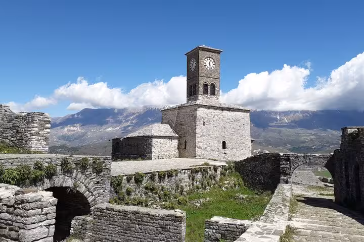 Historic stone clock tower at Gjirokastër Castle with mountainous backdrop, a must-visit on a 6-day Albania tour.